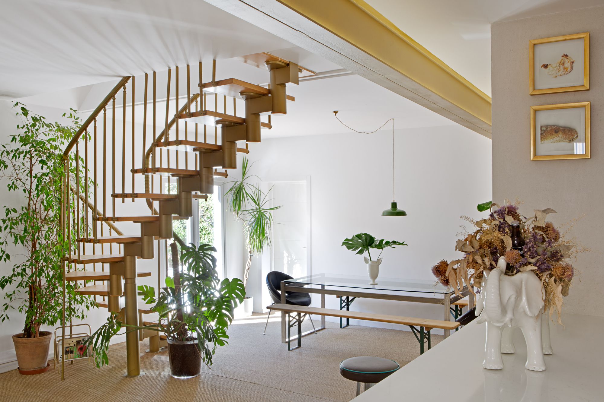 Salón luminoso con escalera de caracol, mesa de cristal y plantas de interior